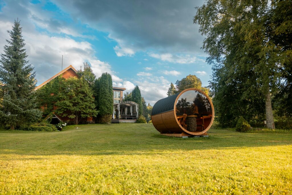 Fasssauna mit Glasfront auf einer Wiese im Garten vor einem Wohnhaus