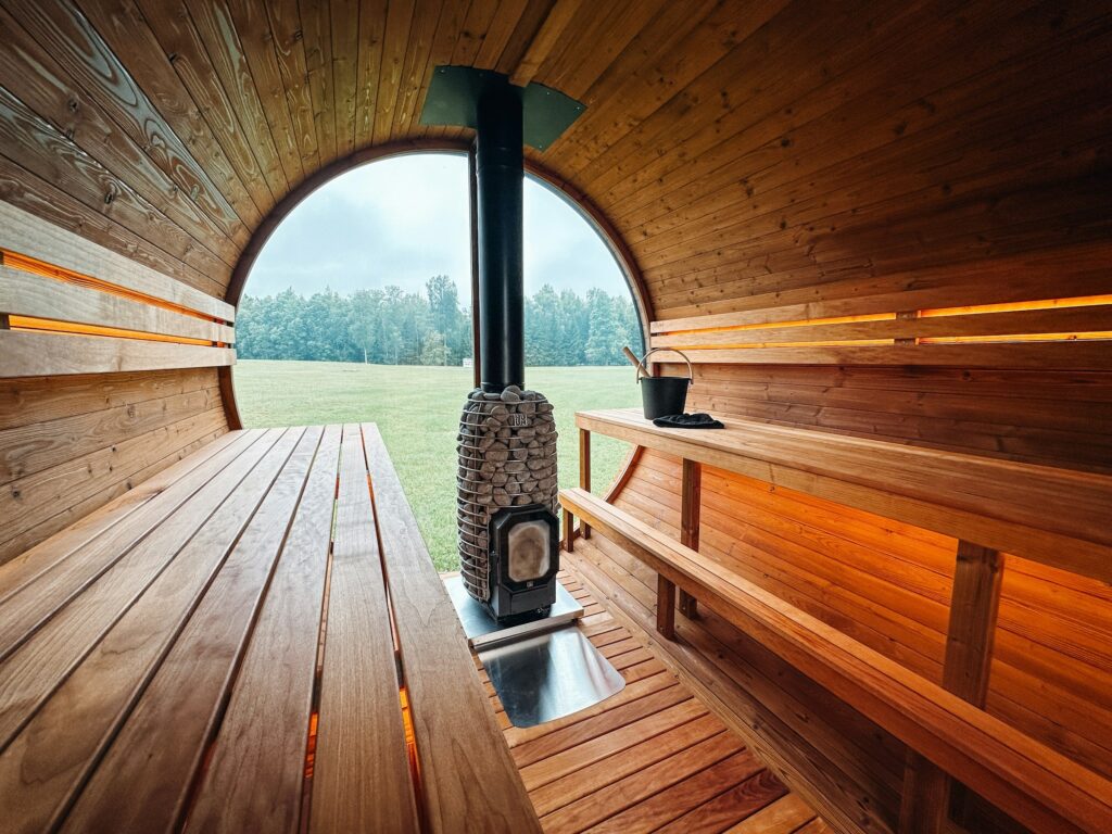 Holzofen mit Ofenrohr in einer Fasssauna vor dem halbrunden Panoramafenster