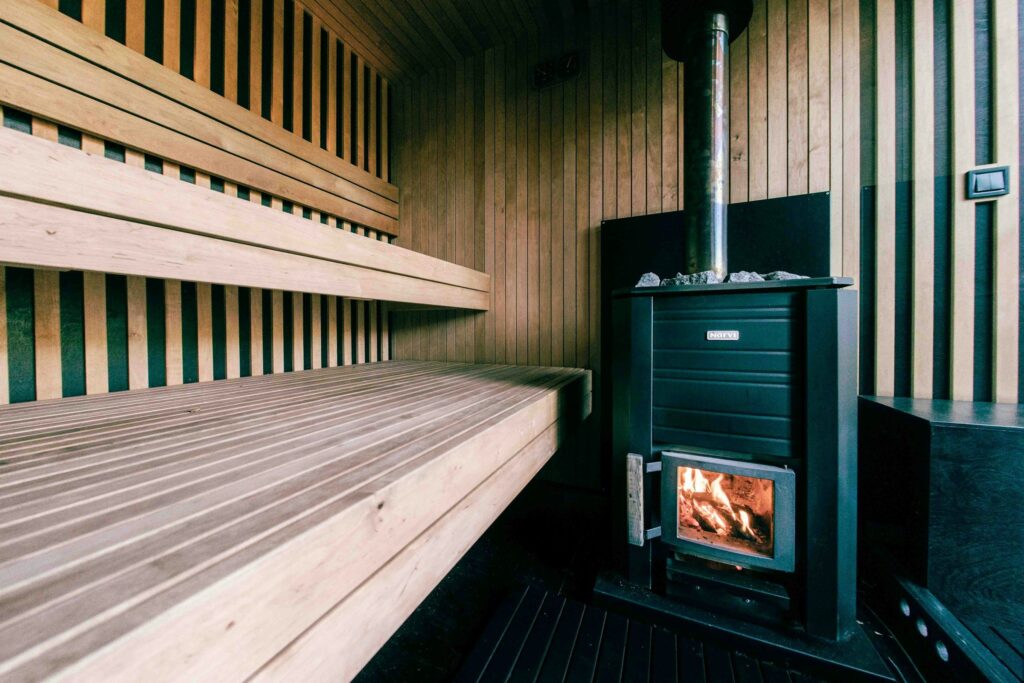 Schwarzer Holz-Saunaofen mit brennendem Feuer hinter dem Sichtfenster und Ofenrohr