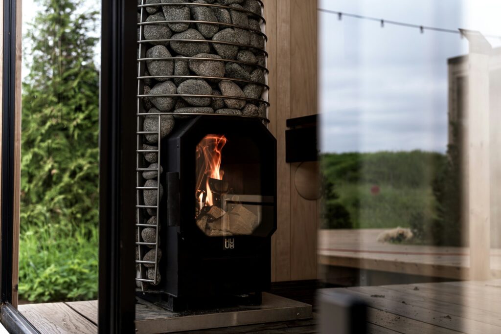 Holzofen mit hohem Steinkorb und Feuer hinter der Glastür in einer Sauna