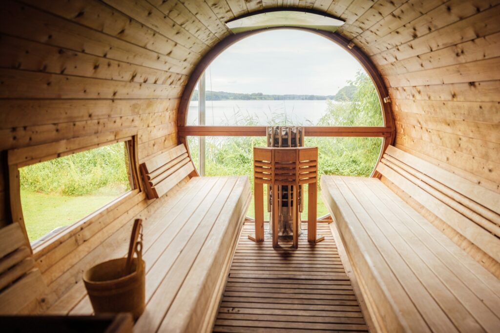 Innenraum einer Fasssauna mit Bänken und Halbrundfenster zum See