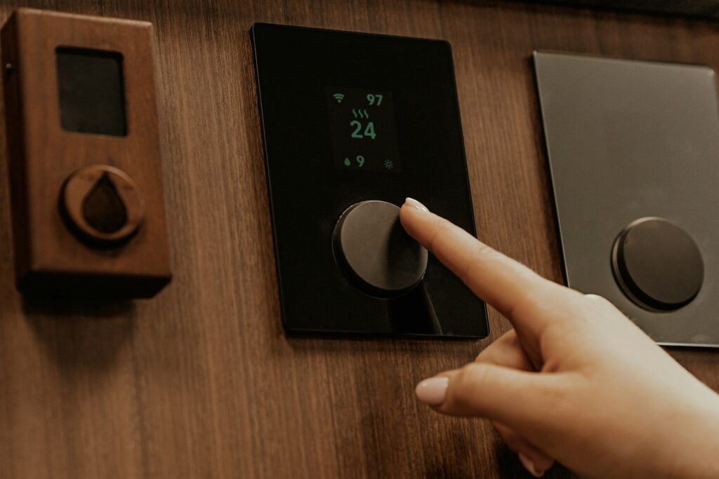 Finger am Drehknopf eines Saunasteuergeräts mit Display an einer Holzwand