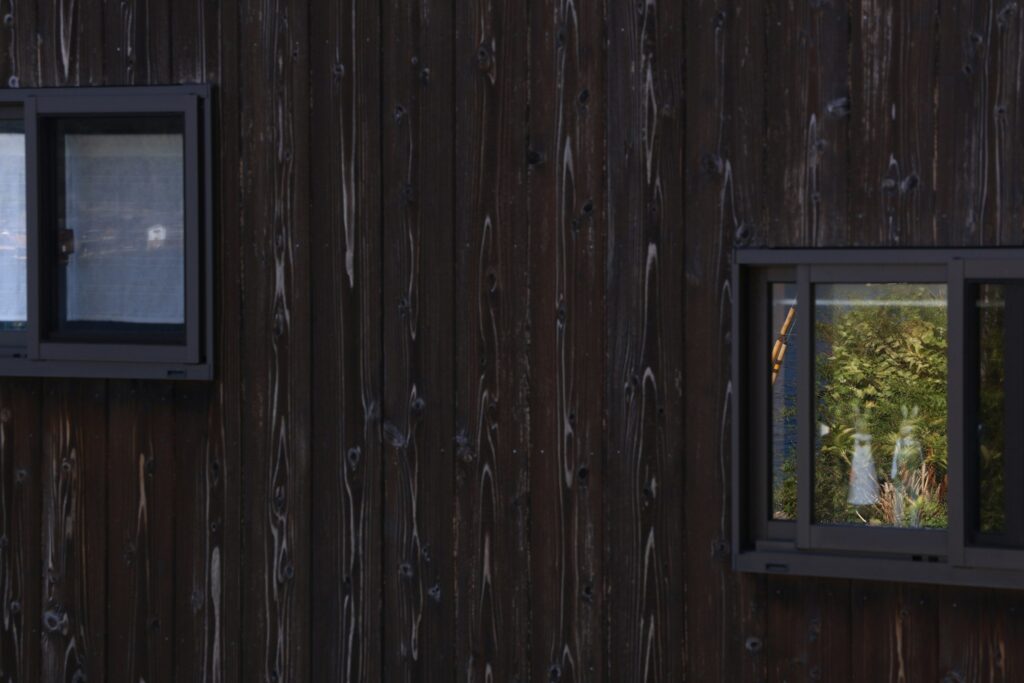 Fassade aus dunkelbraunen Holzbrettern mit zwei Fenstern