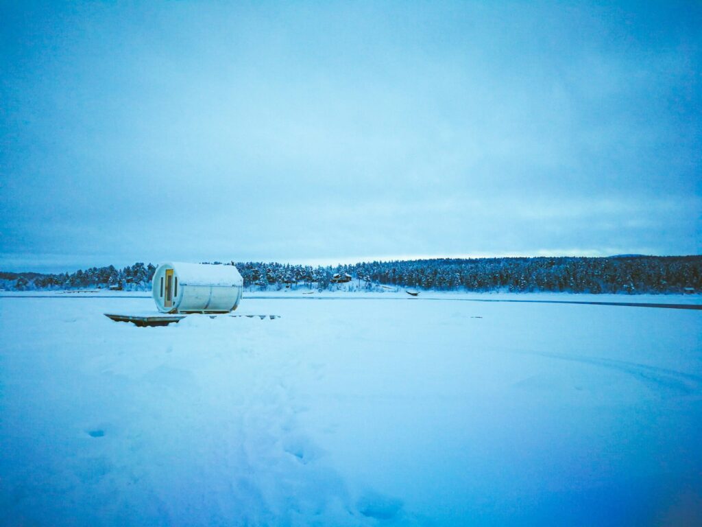 Kleine Fasssauna auf einem zugefrorenen See vor Nadelwald